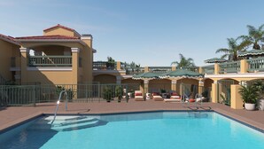 A swimming pool with a tiled deck, a covered seating area with lounge chairs, and a multi-story building with balconies. - Beachside Boutique Hotel + Pool + Hot Tub + Rooftop| The Mara by AvantStay (Laguna Beach)