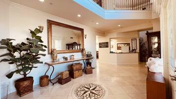 A spacious lobby with a large mirror, potted plants, a console table, and a tiled floor.