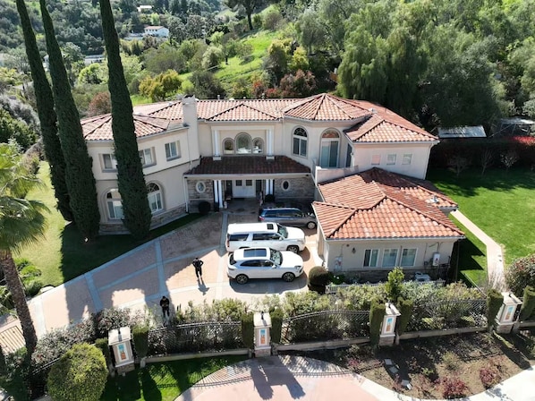 A large, multi-story house with a tiled roof, a driveway with parked cars, and a well-maintained garden. - La Habra Heights Luxury Escape with 7 bedroom (Hacienda Heights)