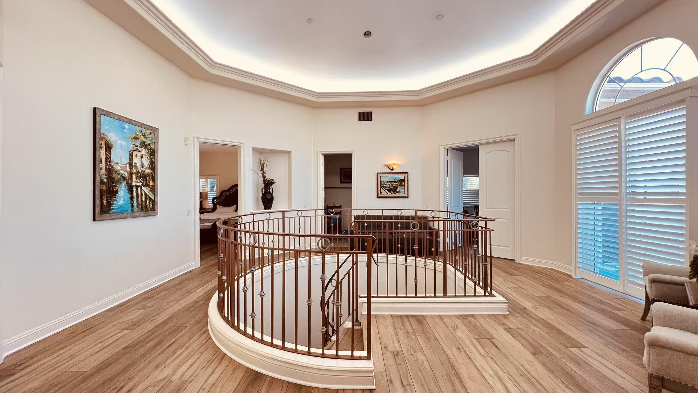 A spacious interior with a central staircase, wooden floors, and a large window with blinds.