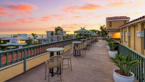 A rooftop terrace with outdoor seating, a view of the ocean, and a sunset sky.