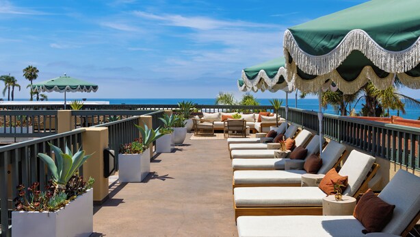 A rooftop lounge area with outdoor seating, potted plants, and a view of the ocean. - 1 Block to Beach | Pool + Hot Tub + Rooftop Terrace | The Mara by AvantStay (Laguna Beach)