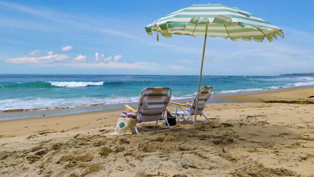 A beach with two striped beach chairs and a green and white striped umbrella.