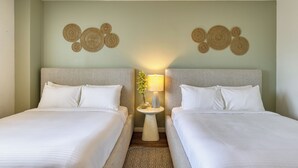 Une chambre d’hôtel avec deux lits, une petite table de chevet avec une lampe, des œuvres d’art décoratives au mur et un tapis à motifs.