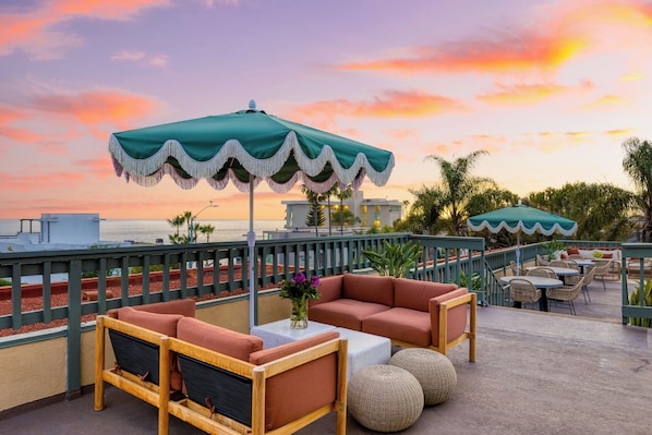 A rooftop terrace with outdoor seating, a view of the ocean, and a sunset sky. - Rooftop Ocean Views + Pool + Hot Tub + Walk to Beach | The Mara by AvantStay (Laguna Beach)