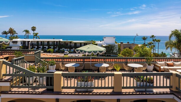 A resort with outdoor seating, palm trees, and a view of the ocean.