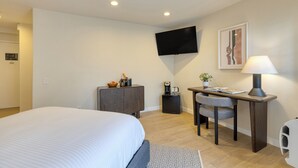 A hotel room with a bed, a desk with a chair, a television mounted on the wall, and a small cabinet. - Boutique Stay + Pool + Hot Tub + Rooftop | Walk to Beach + Dining + Galleries (Laguna Beach)