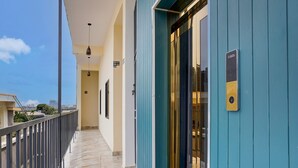 A corridor with a marble floor, a blue door with a keypad, and a balcony with a railing. - Deluxesree Residency (Bengaluru)