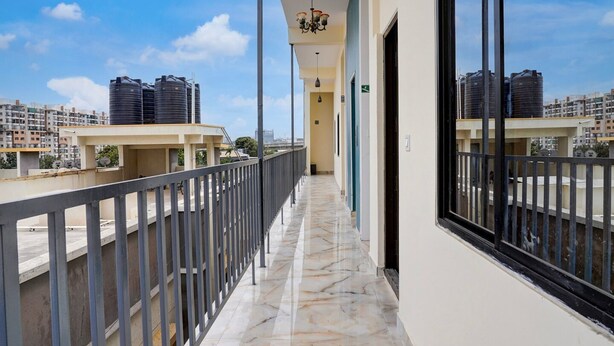 A corridor with a marble floor, a balcony with a metal railing, and a view of other buildings. - Deluxesree Residency (Bengaluru)