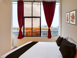 A hotel room with a large window, a bed with black and white bedding, and a city view. - Deluxesree Residency (Bengaluru)