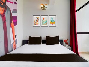 A modern hotel room with a large bed, two pillows, a nightstand with a vase, and three framed artworks on the wall. - Deluxesree Residency (Bengaluru)