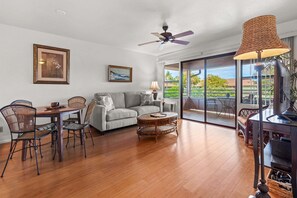 Ein Wohnzimmer mit Sofa, Esstisch, Stühlen, Deckenventilator und Blick durch große Glasüren.