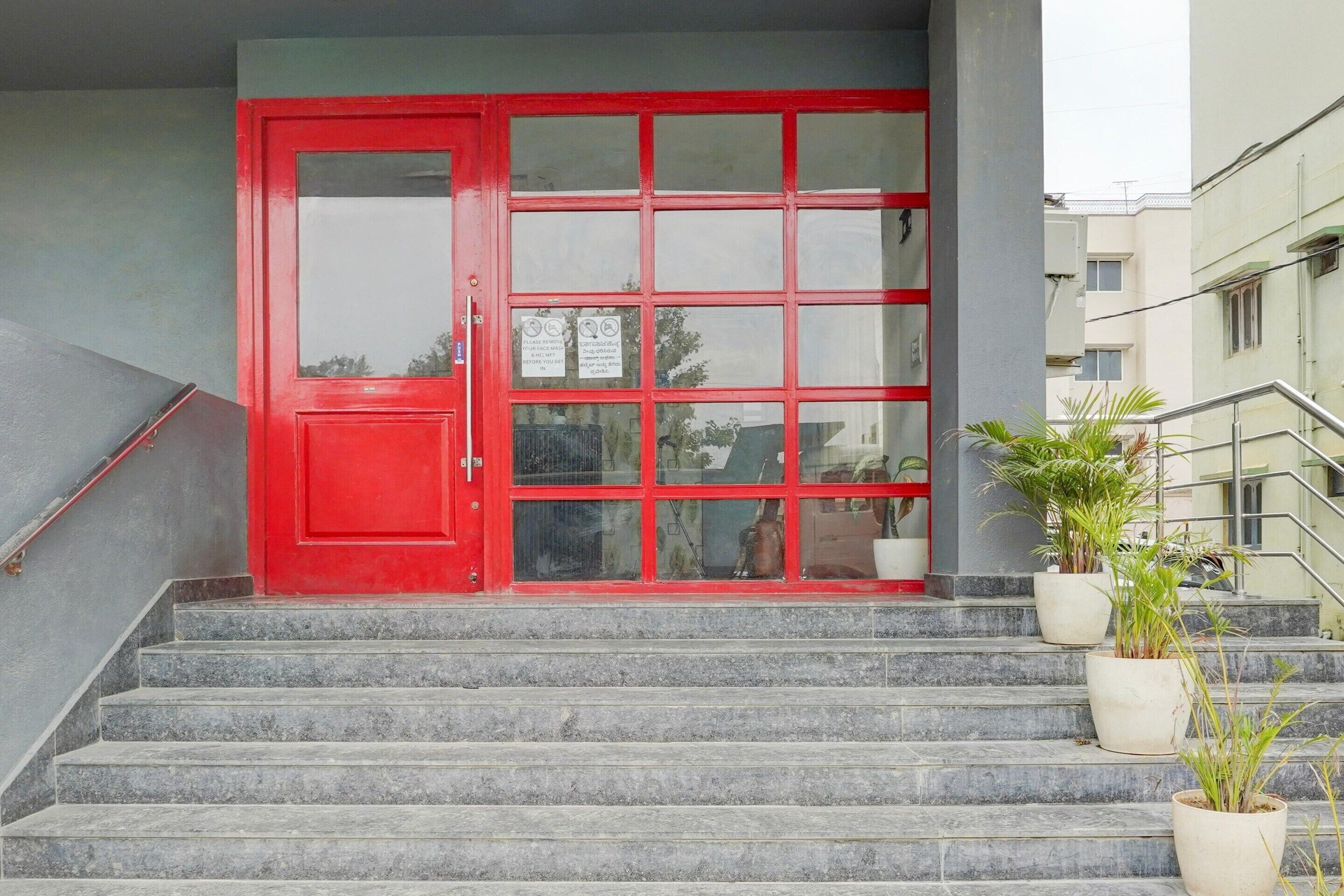A red door with glass panels, a set of stone steps, and potted plants on the landing.