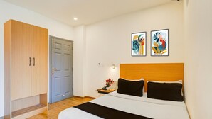Un dormitorio con una cama, un armario, una mesita de noche con una lámpara y dos obras de arte colgadas en la pared.