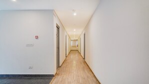 Un pasillo largo y estrecho con suelo de madera, paredes blancas y puertas a ambos lados.