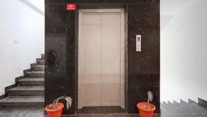 Un ascensor con un cartel de 'No Fumar', un extintor y dos plantas en el suelo.