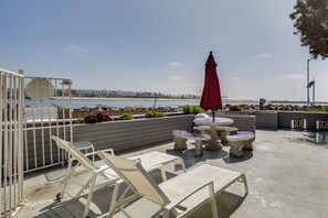 An outdoor patio with lounge chairs and a table, overlooking a beach and ocean. - Waterfront Condo: Beach, Bay & Active Jetty Views (San Diego)