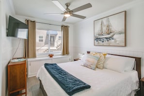 A bedroom with a bed, a ceiling fan, a TV, a window with curtains, a painting, and a bedside table. - Waterfront Condo: Beach, Bay & Active Jetty Views (San Diego)