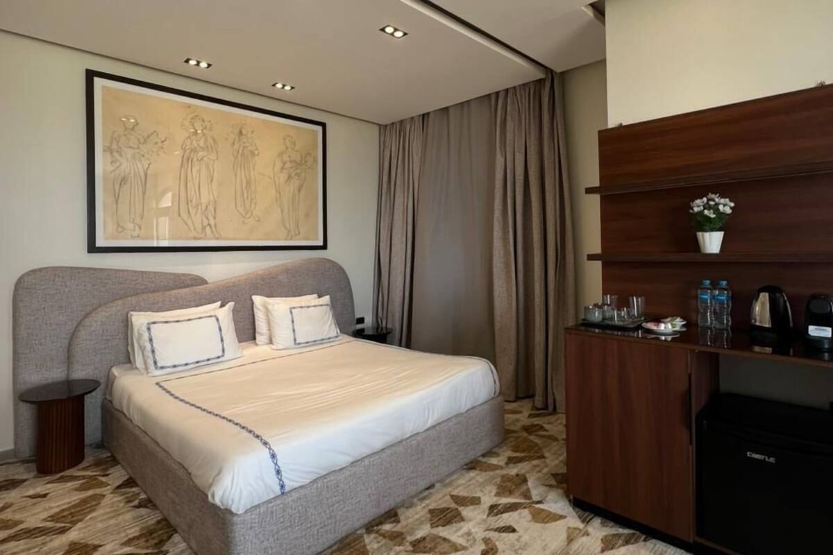 Una habitación de hotel moderna con una cama grande, un escritorio, una cafetera y una obra de arte enmarcada en la pared.