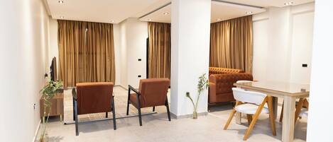 A modern hotel room with a dining area, a sofa, and a TV.