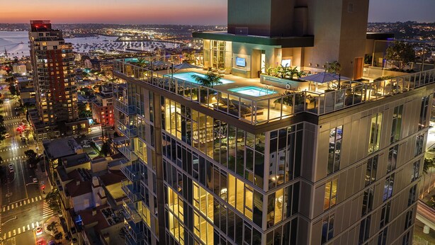 Un hotel di grandi dimensioni con piscina sul tetto, ampie finestre e vista sulla città al crepuscolo.