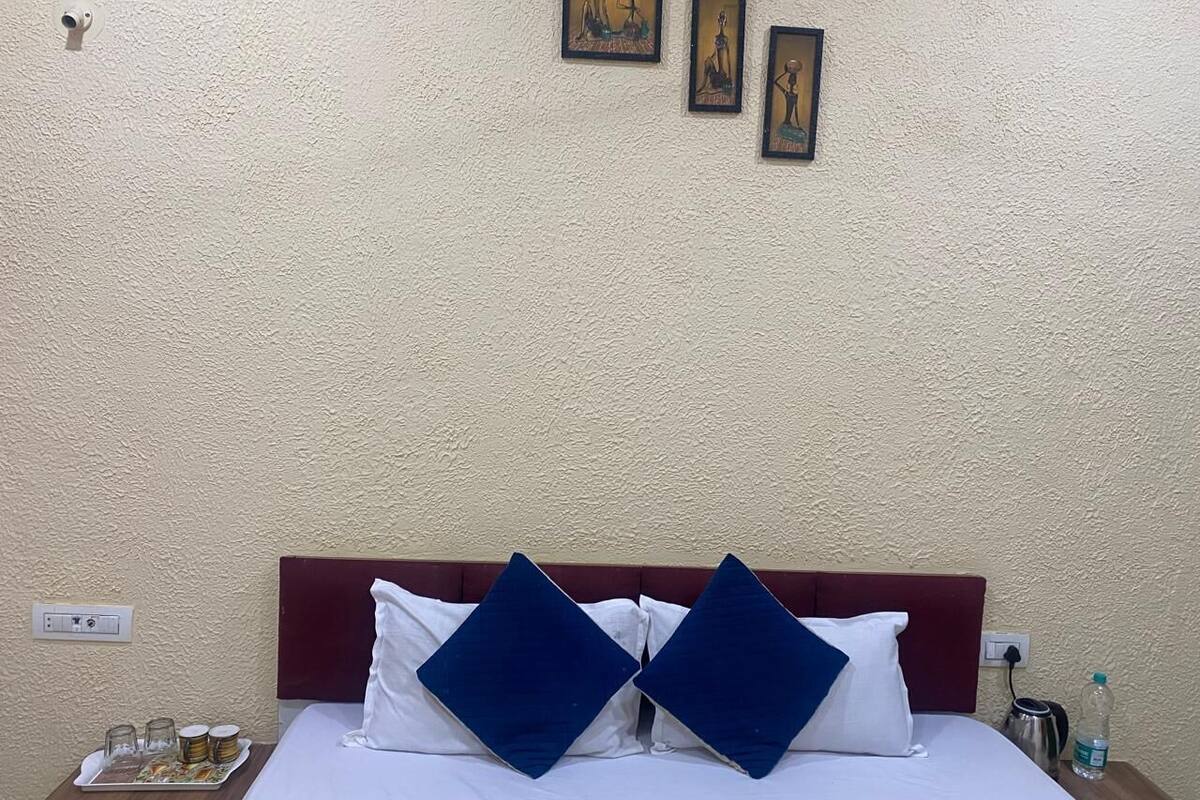 A hotel room with a bed, two pillows, a nightstand, a wall-mounted picture, and a power outlet.