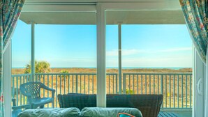 Un balcone con vista sulla spiaggia, arredi in vimini e una sedia di plastica.