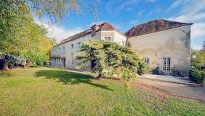 Ein zweistöckiges Gebäude mit Garten, einem großen Baum und blauem Himmel.