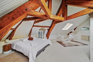 A bedroom with a sloped ceiling, a bed, a chair, a table, and a radiator.