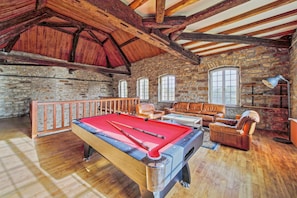 A pool table with cues, a leather sofa, and a stone wall.