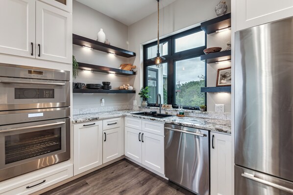 A modern kitchen with stainless steel appliances, white cabinetry, and a window overlooking greenery.