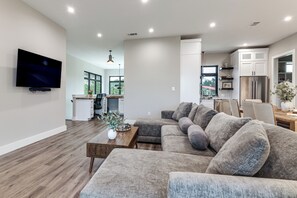 A modern living room with a sectional sofa, a coffee table, and a flat-screen TV mounted on the wall.