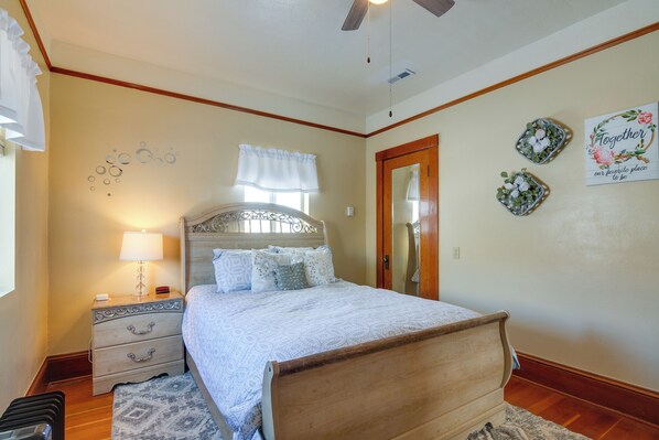 A bedroom with a wooden bed, a nightstand with a lamp, a dresser, and decorative wall art. - Historic Bryce Canyon Basecamp w/ Game Room! (Cannonville)