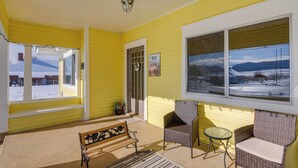 Une pièce jaune avec un banc, deux fauteuils en osier, une petite table et une grande fenêtre donnant sur un paysage enneigé.