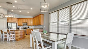 A kitchen with wooden cabinets, a dining table with chairs, a clock, and a window with blinds. - Poolside Oasis: Group-Friendly Getaway in Phoenix! (Phoenix)