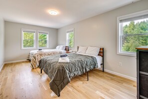 A bedroom with two beds, a wooden floor, and large windows with a view of trees. - Explore the White Mountains! Spacious Rural Home (Thornton)