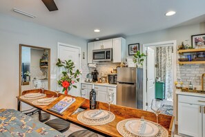 A modern kitchen with white cabinets, a stainless steel refrigerator, and a dining area with a wooden table set for two.