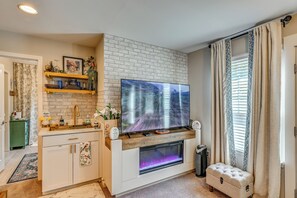 A modern living room with a flat-screen TV mounted on a brick wall, a fireplace with a glass front, and a small seating area.