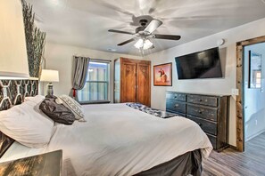 Une chambre à coucher comprenant un lit, un ventilateur de plafond, une télévision, une armoire en bois et une fenêtre avec des rideaux.