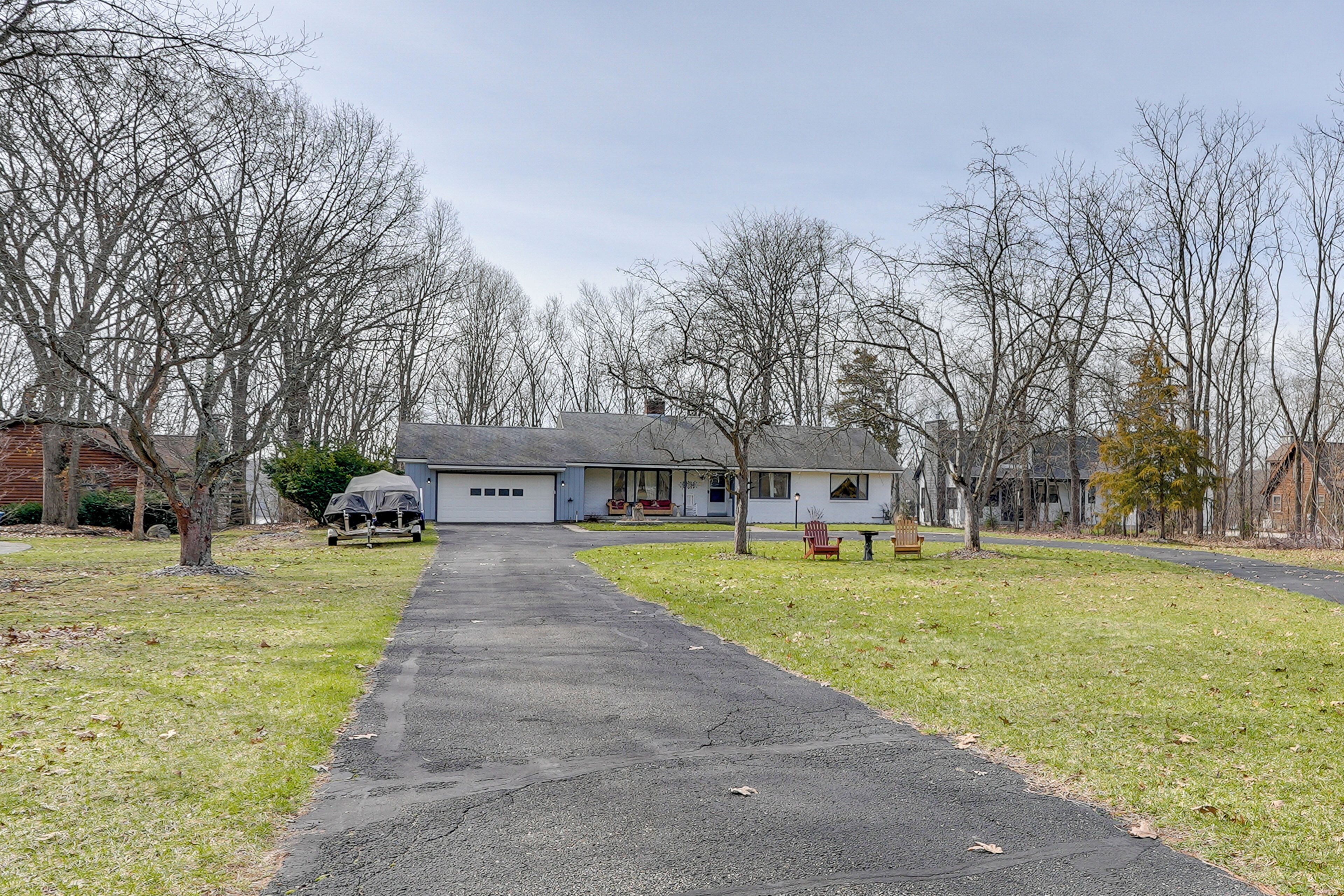 A residential driveway leading to a single-story house with a garage, surrounded by leafless trees and a grassy lawn.