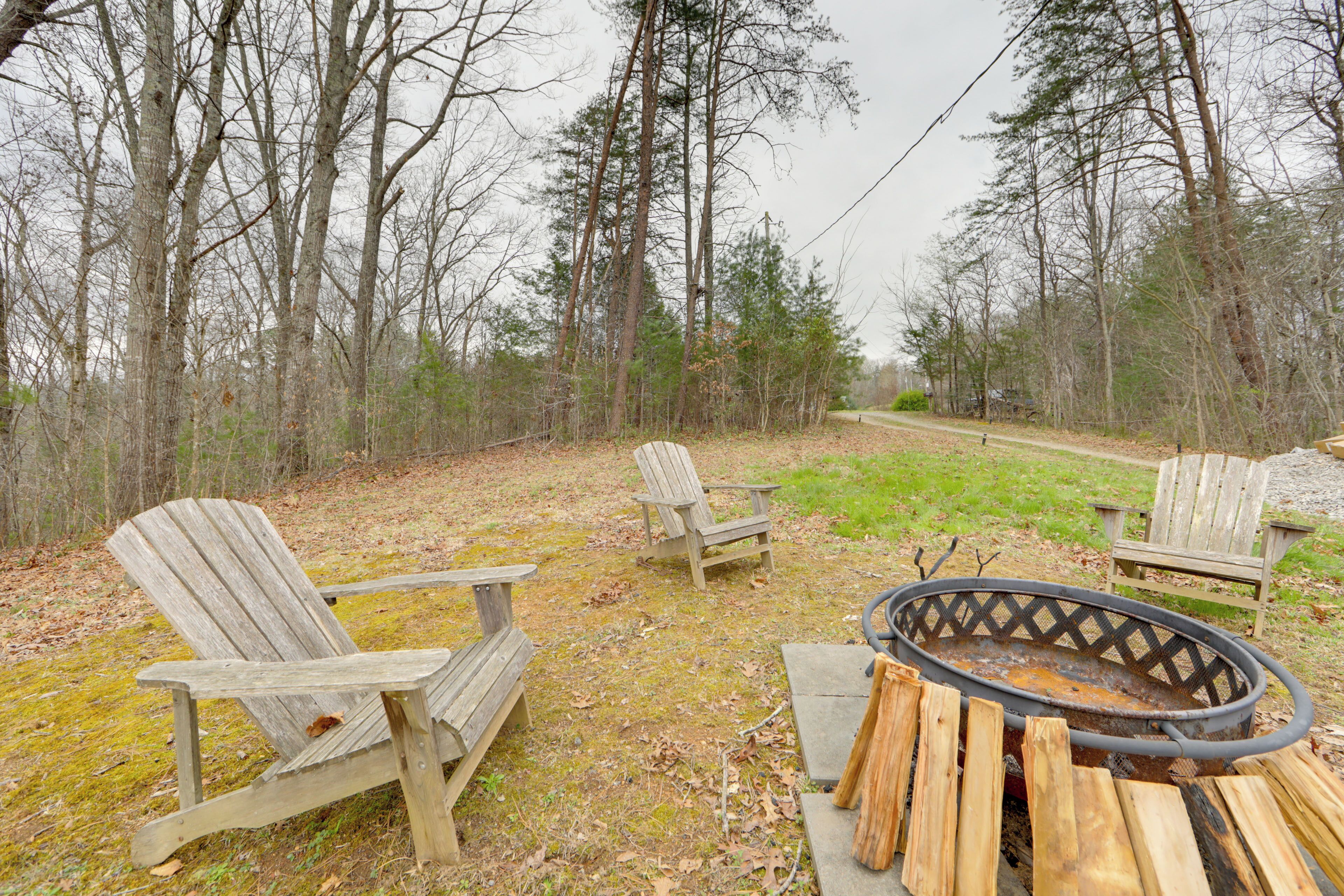 A campsite with two Adirondack chairs, a fire pit, and a gravel path.