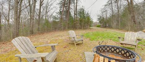 A campsite with two Adirondack chairs, a fire pit, and a gravel path.