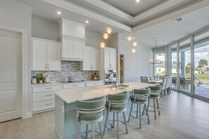 A modern kitchen with white cabinets, a large island with bar stools, and a dining area with a view. - Luxe Canal-Front Getaway w/ Pool in Punta Gorda! (Punta Gorda)