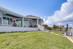 A modern house with large windows, a covered patio, and a grassy lawn. - Luxe Canal-Front Getaway w/ Pool in Punta Gorda! (Punta Gorda)