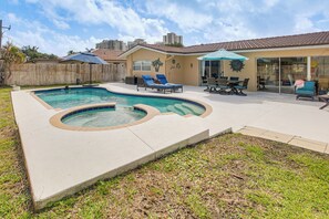 A backyard with a swimming pool, lounge chairs, and a patio area.
