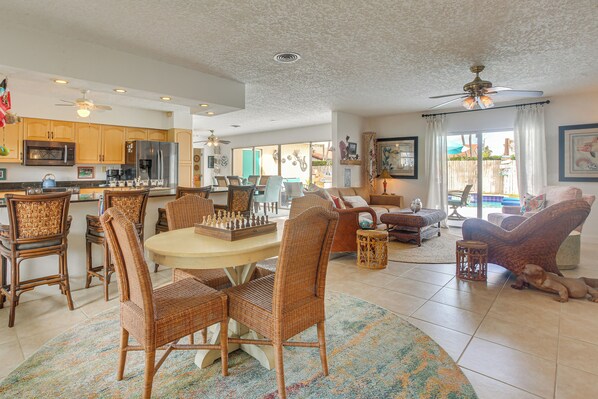 A spacious living room with a dining area, wicker furniture, a ceiling fan, and a view of the outdoors.