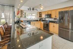 A kitchen with granite countertops, stainless steel appliances, wooden cabinets, and a ceiling fan.