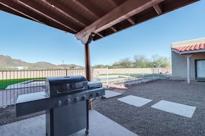 Eine überdachte Terrasse mit Grill, Pool und Bergblick.