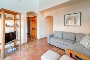 Ein Wohnzimmer mit grauem Sofa, einem Holz-TV-Schrank, einem gerahmten Bild an der Wand und einem Fliesenboden.