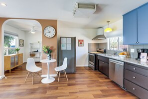 A modern kitchen with wooden flooring, white chairs, a dining table, and blue cabinets. - Pet-Friendly Desert Retreat w/ Hot Tub in Landers! (Landers)